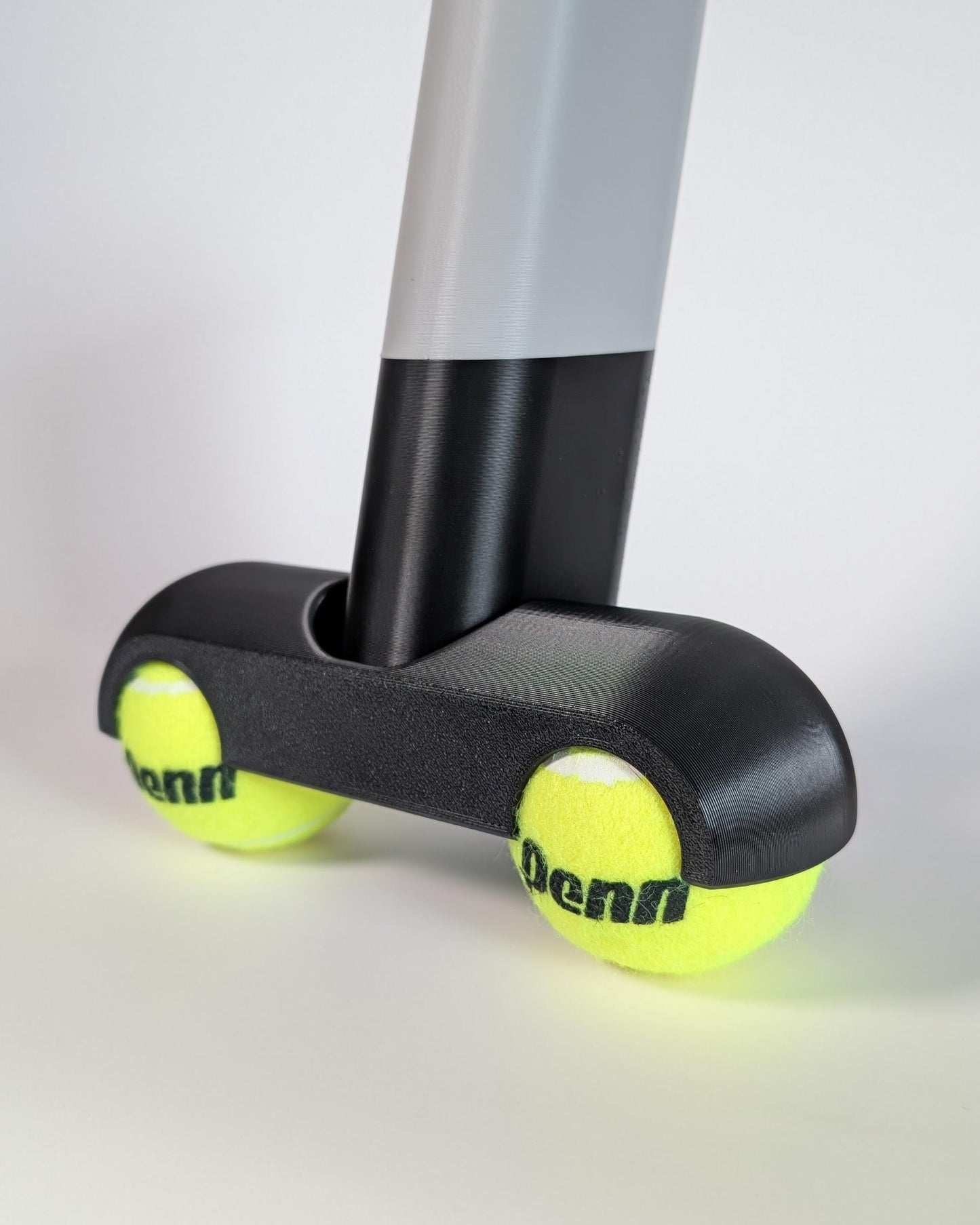 Rocker Foott with two yellow tennis balls attached to a gray and black stand on a light gray background.
