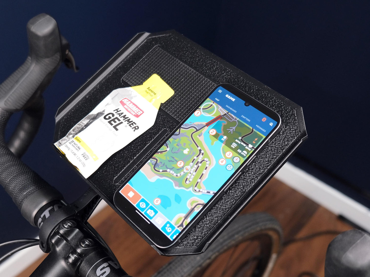 trainer tray with grippy surface holding a hammer gel and a phone displaying zwift companion app