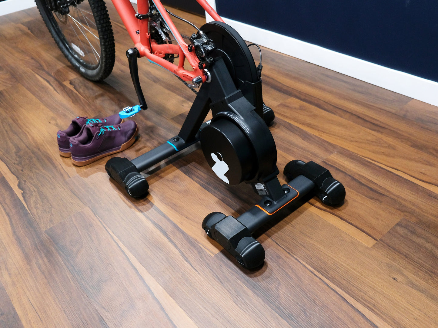 Bicycle trainer on a wooden floor with a bicycle, tennis balls, and shoes nearby