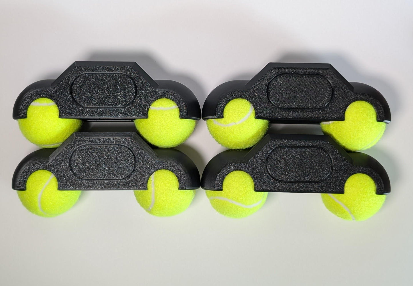 Four black tennis ball holders with yellow tennis balls on a white background