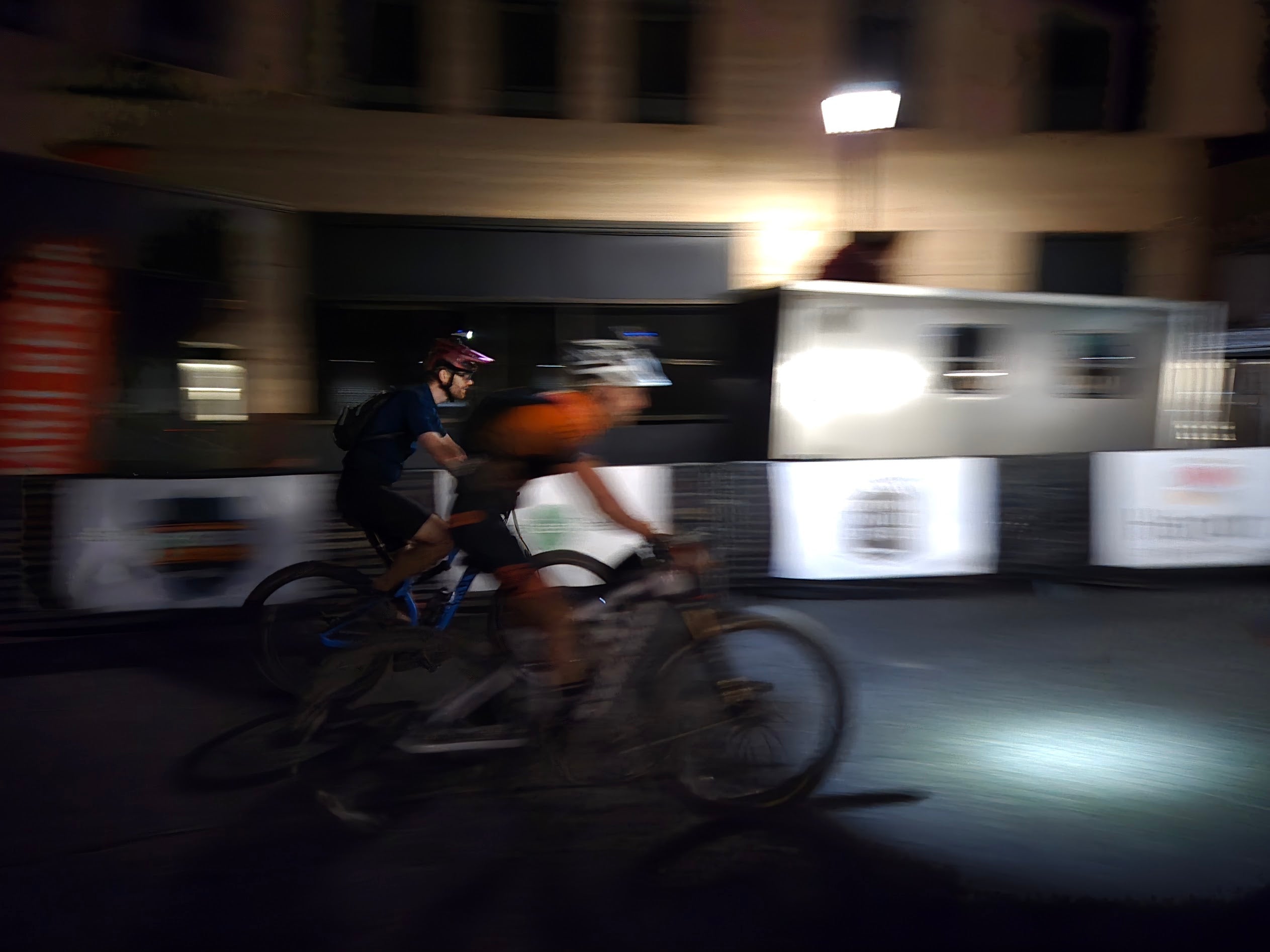 Two cyclists riding bicycles on a city street at night.