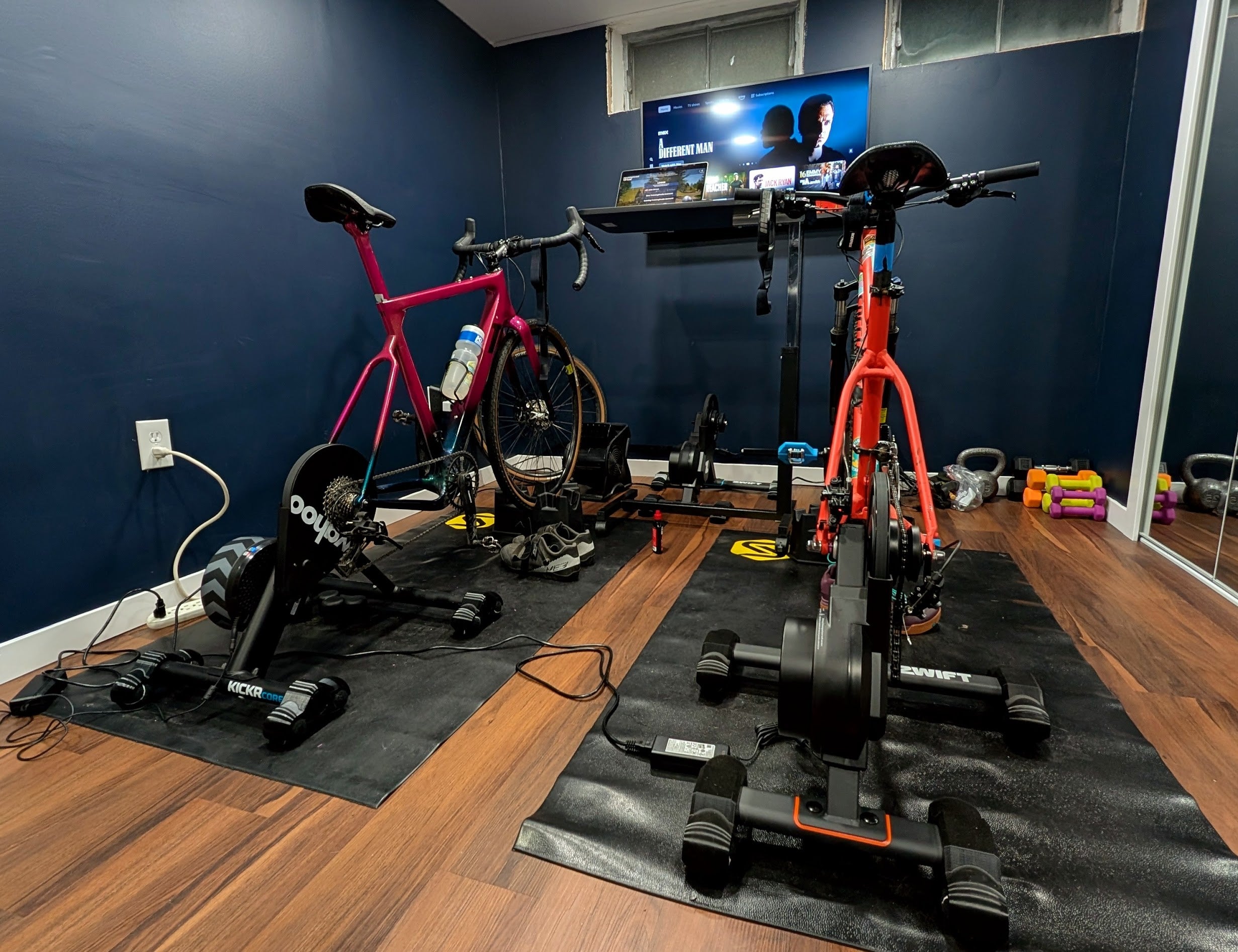 Home gym with stationary bikes and a television on a blue wall.