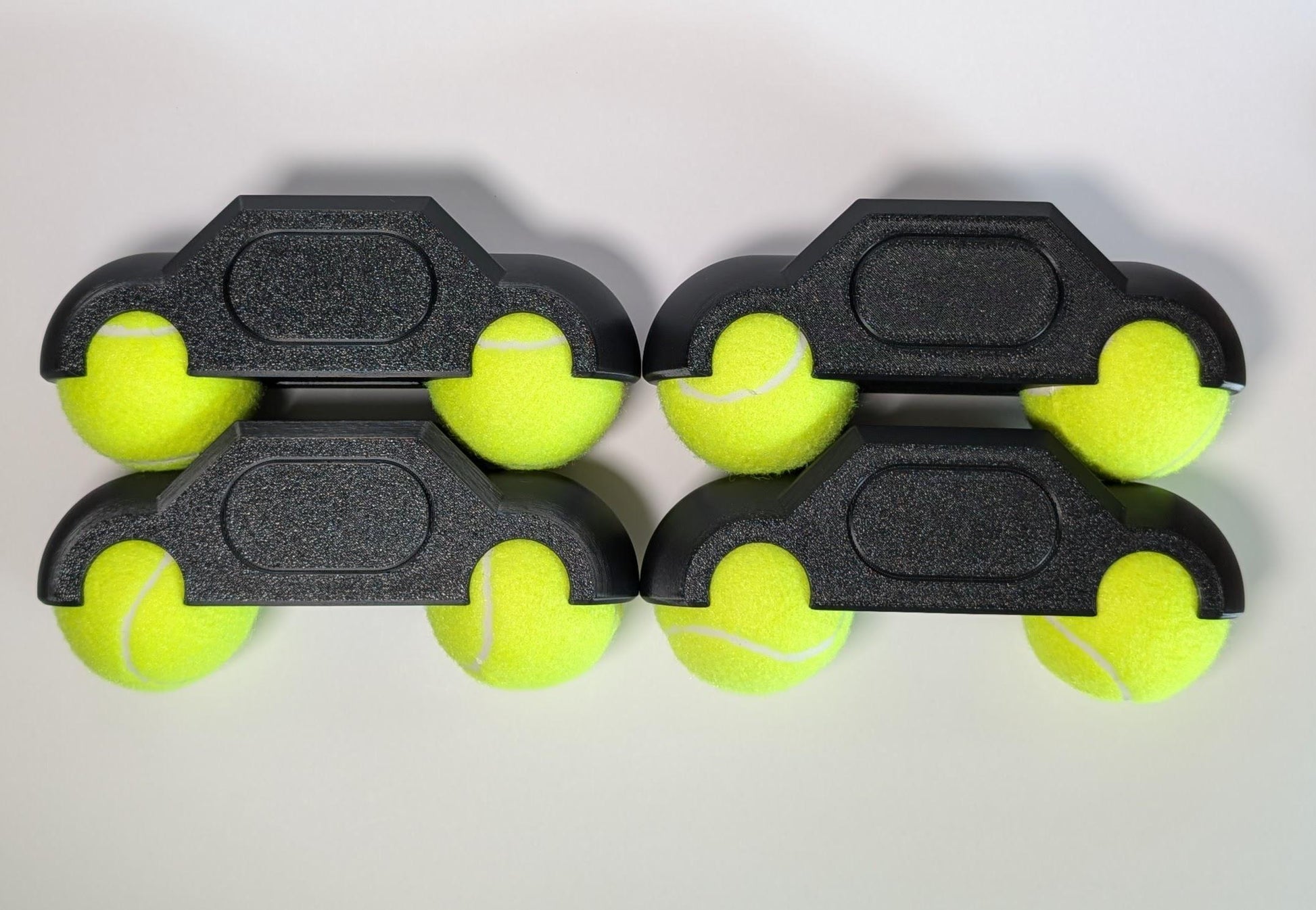 Four black tennis ball holders with yellow tennis balls on a white background